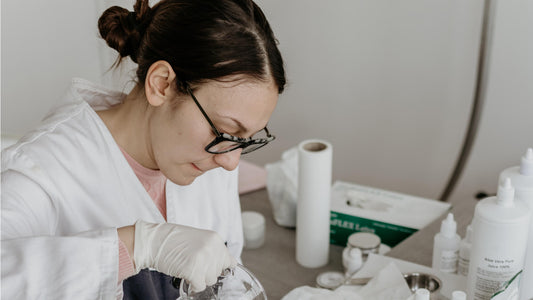 Woman wearing a white lab lab coat pouring a mixture into a skincare bottle