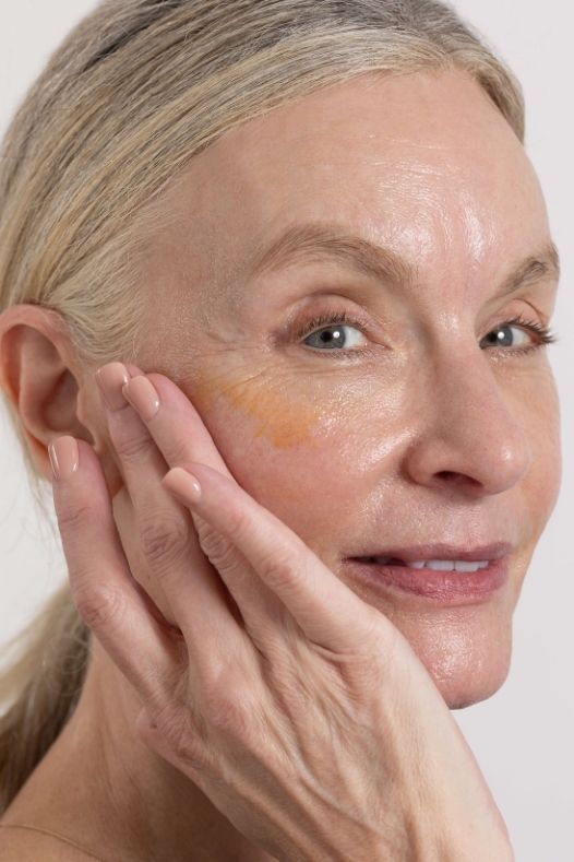 Woman applying perimenopause and menopause skincare product to her face with a neutral background