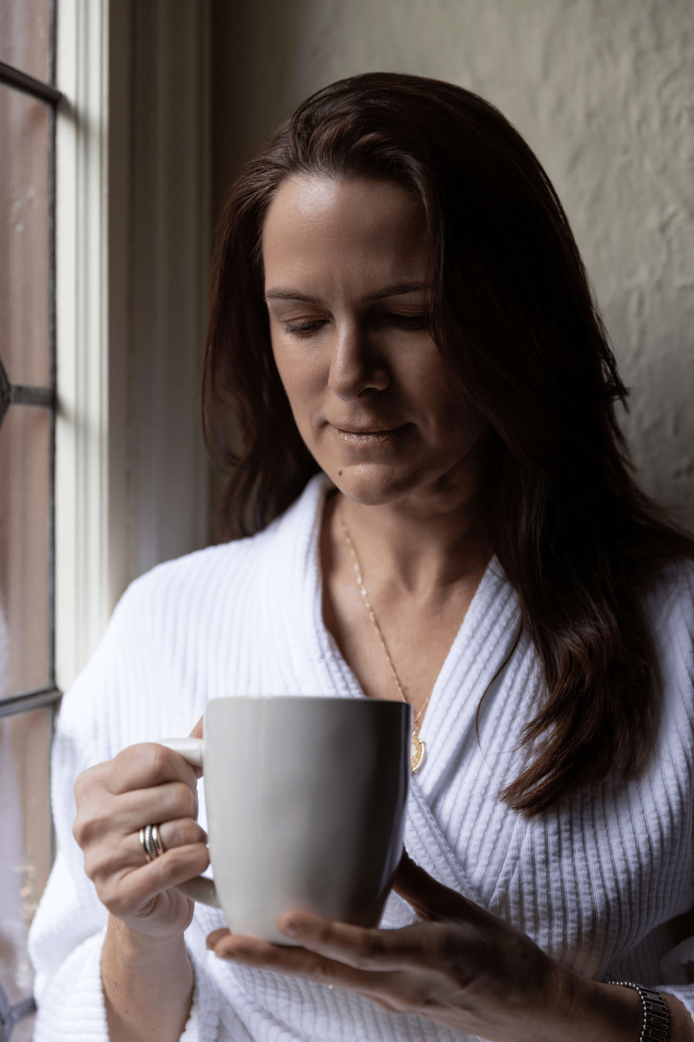 Woman in robe sitting near window drinking tea