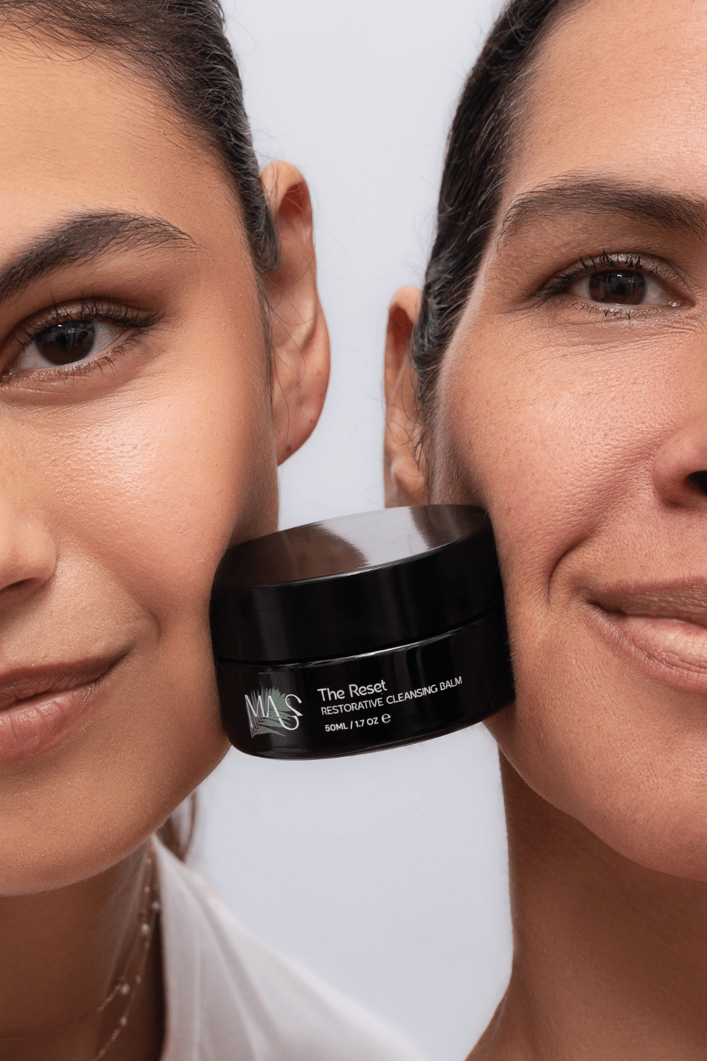 close up of 2 women's faces with black jar of The Reset cleanser in between
