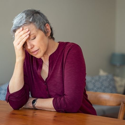 Middle aged woman with eyes closed and hand on her head in a show of stress