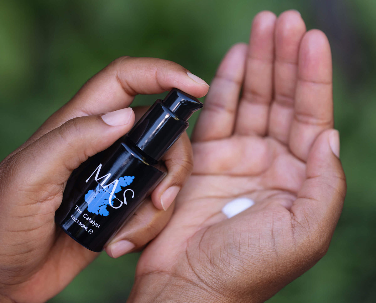Hand holding a Catalyst black bottle labeled with white colored skin serum product dispensed in palm