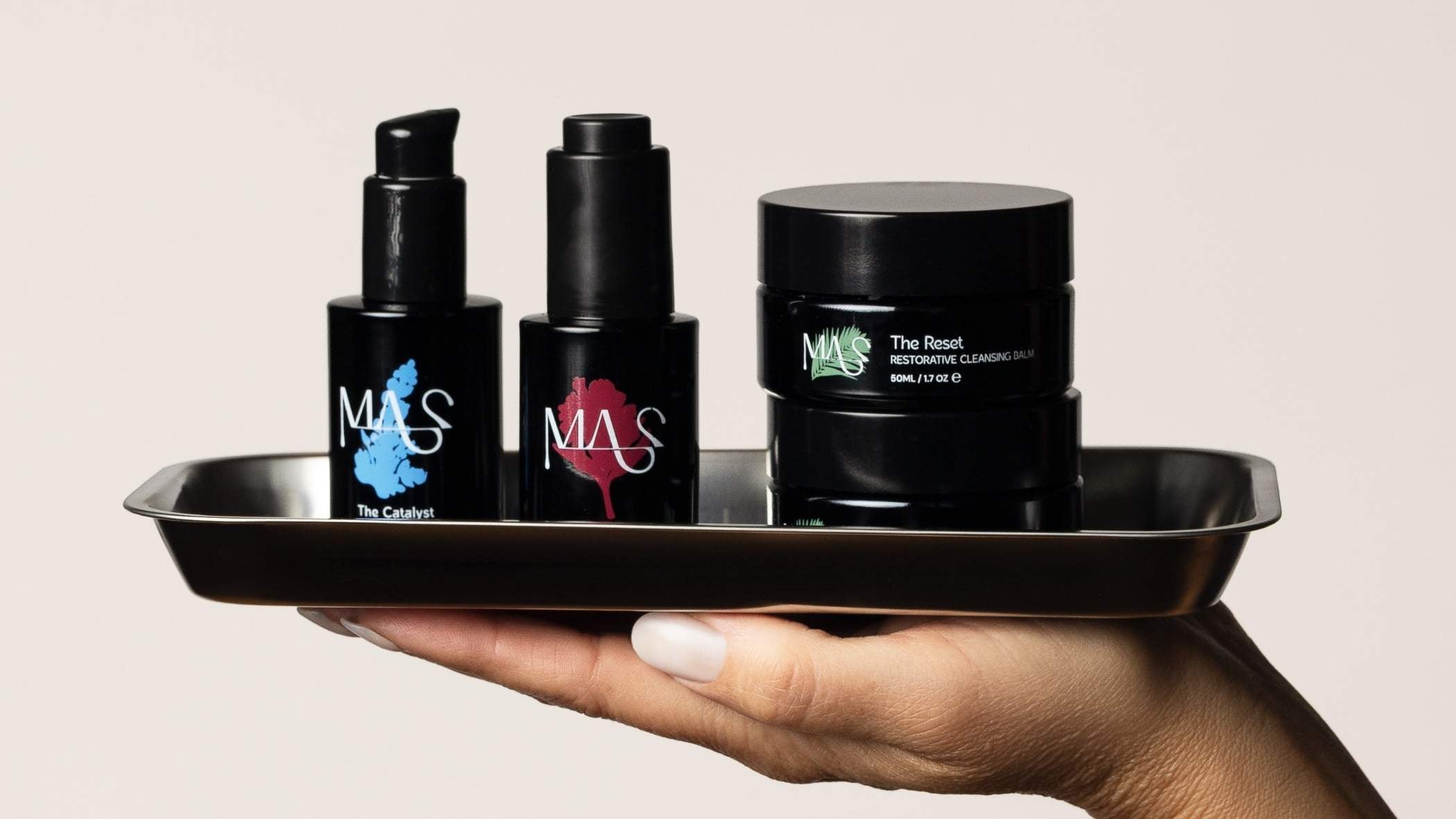 Hand holding a tray with black cosmetic containers featuring 'MAS' branding.